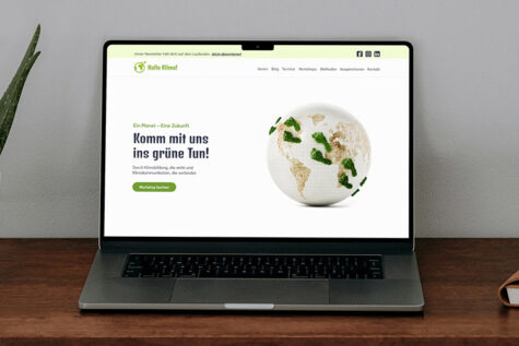 Auf einem Holztisch steht ein Notebook, das die Startseite der Hallo Klima!-Website zeigt.